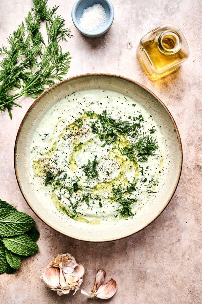 bowl of tzatziki with fresh ingredients around it