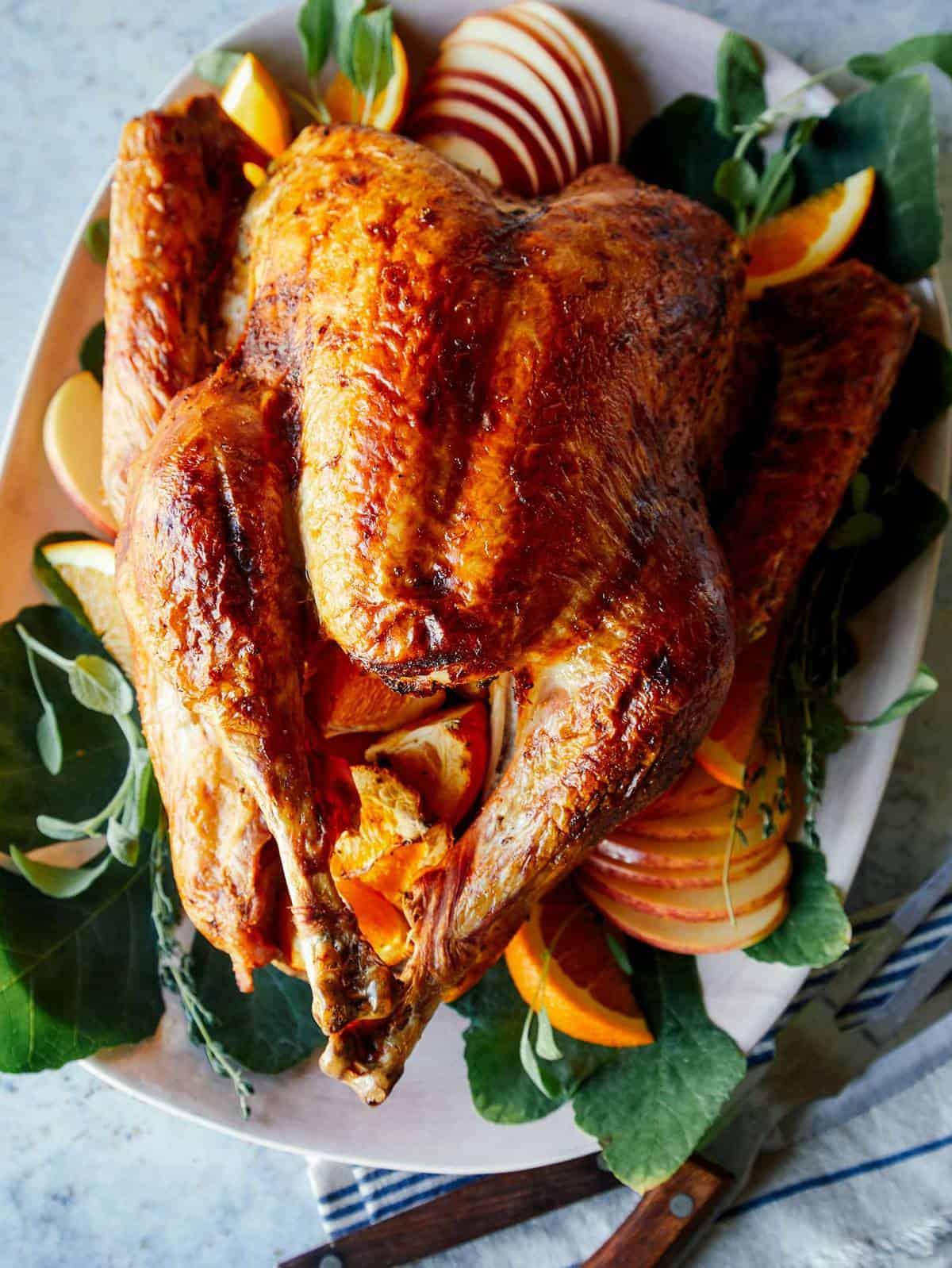 whole roasted golden brown citrus brined turkey on a rustic wooden table with fall decorations
