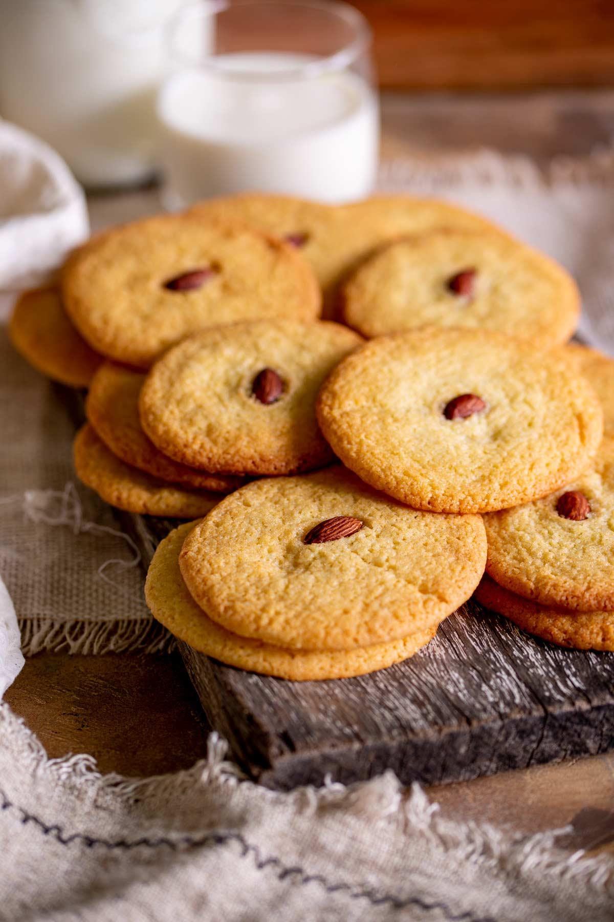 stack of golden almond cookies on a rustic wooden board with a cup of tea