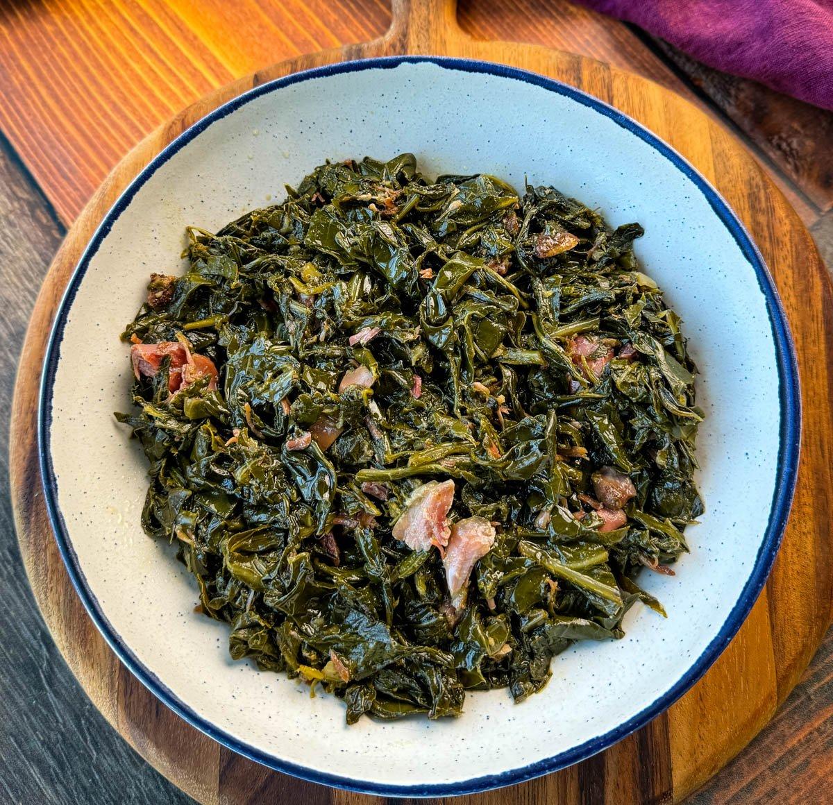 Close up of a bowl of collard greens with ham hocks, showing the texture and color.
