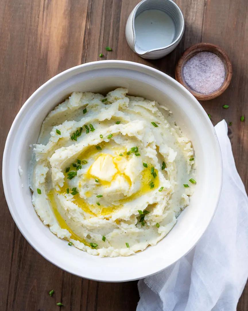 Top-down shot of creamy mashed potatoes with a beautiful melted butter swirl and fresh chives, on a rustic wooden table.