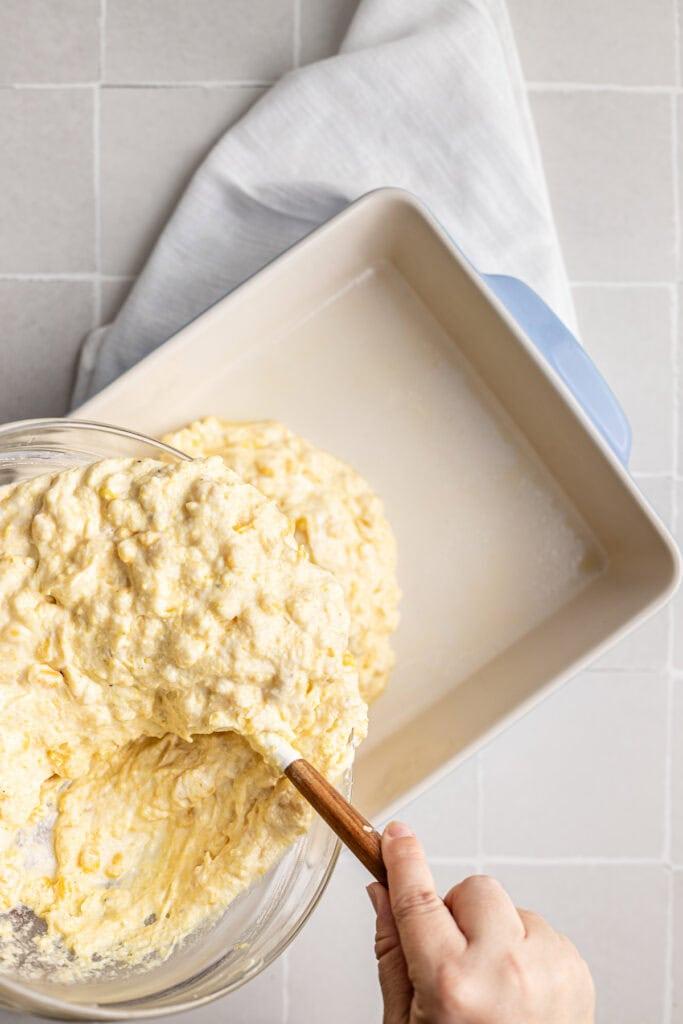 hand serving a slice of corn casserole from a baking dish