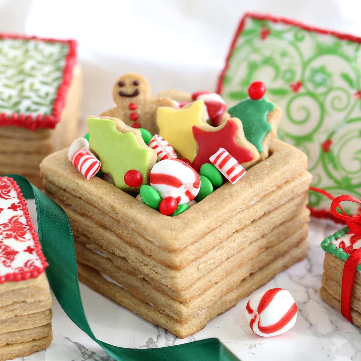 A person carefully placing a plate of frosted fir gingerbread cookies into a beautifully wrapped gift box.