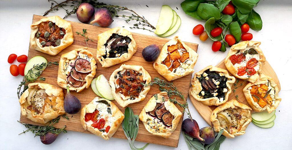 overhead shot of mini cheese tarts arranged on a rustic wooden board with fresh herbs