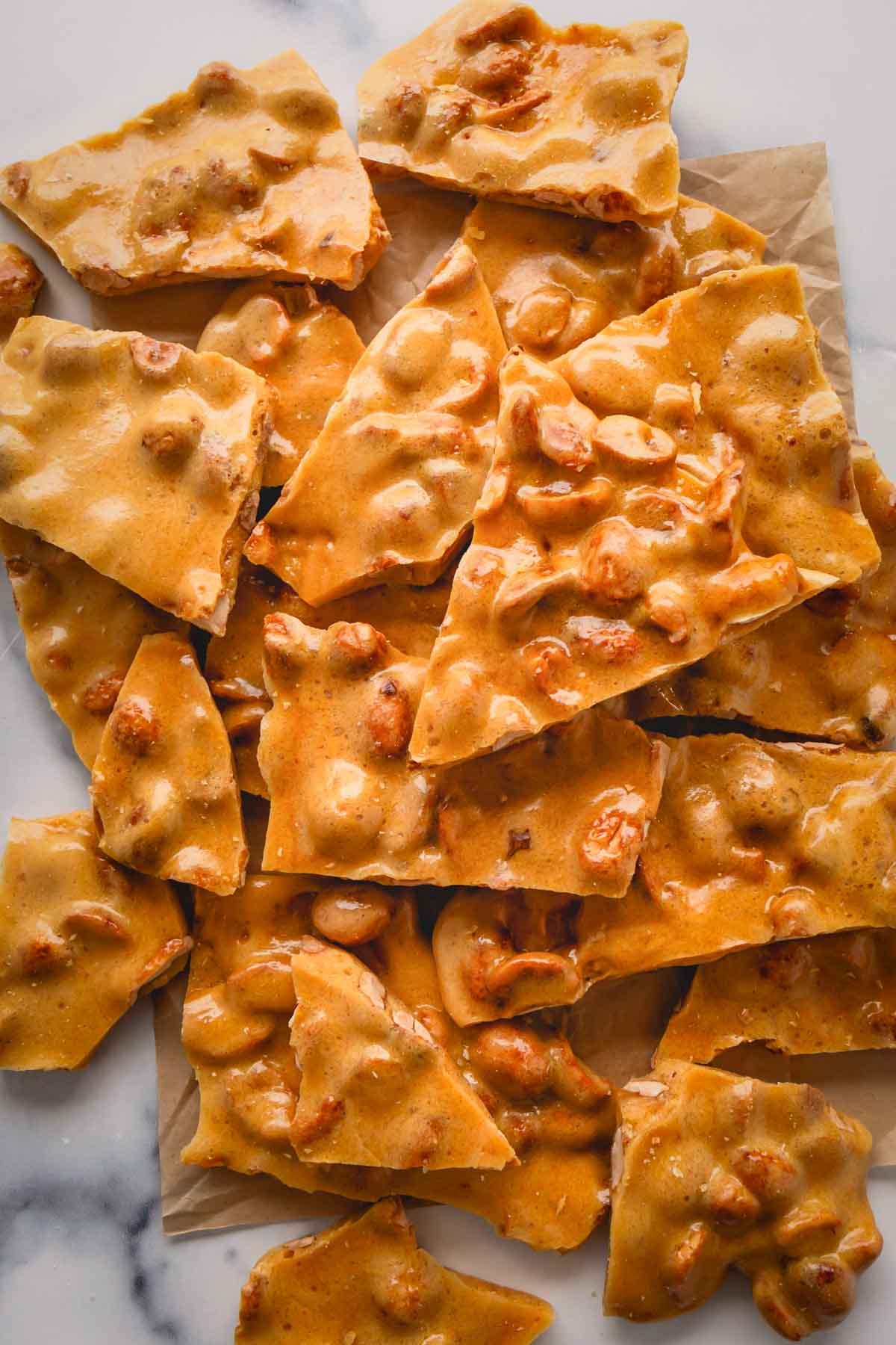 Close-up of golden peanut brittle with a glossy, crunchy texture, broken into pieces on parchment paper
