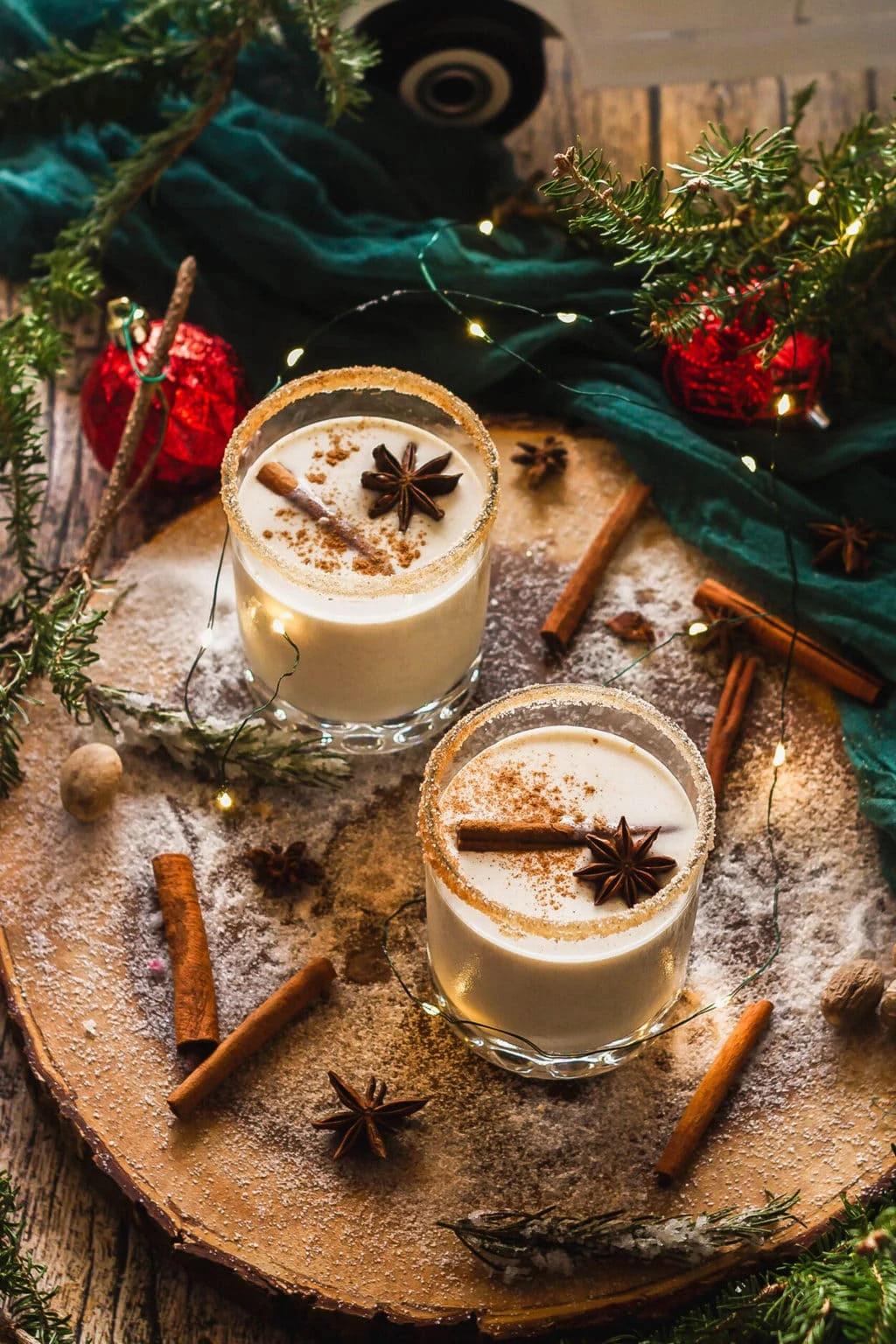 Homemade Coquito in a festive glass, garnished with cinnamon stick and grated nutmeg, surrounded by holiday decorations