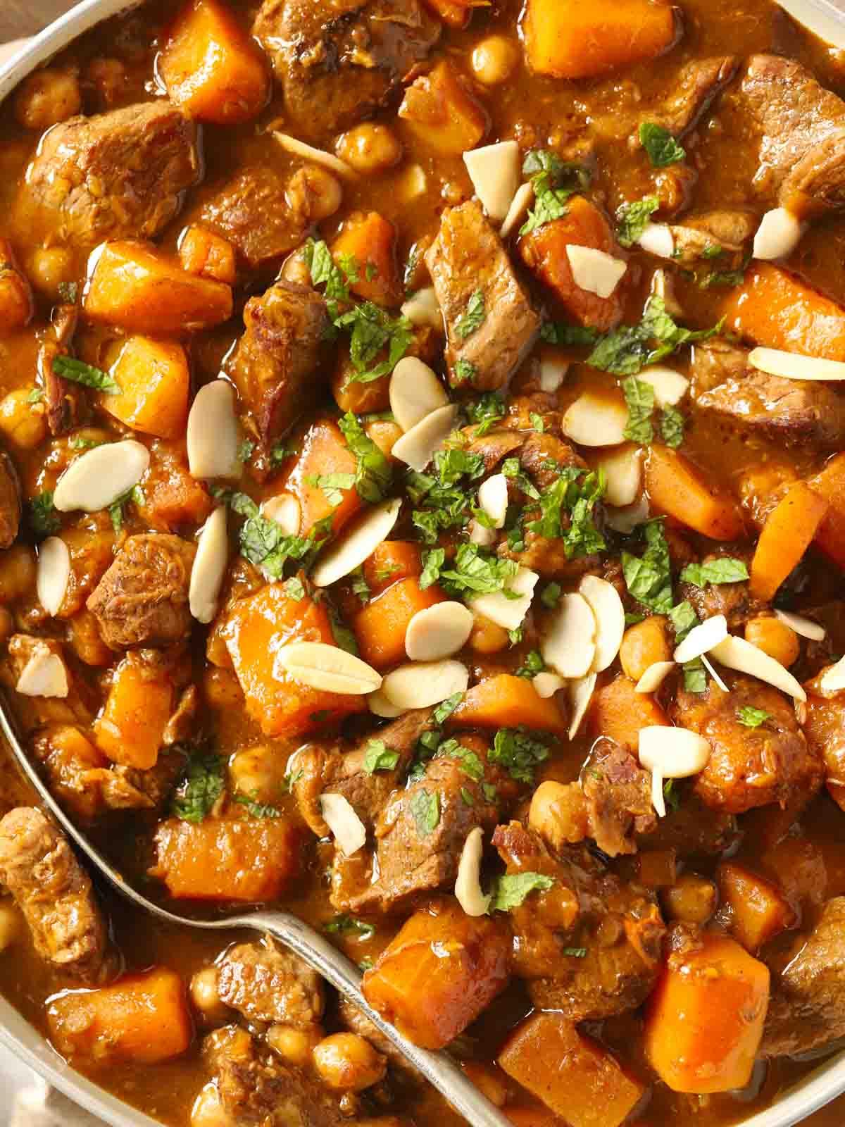Close-up of tender lamb pieces in a rich, cumin-spiced tagine sauce with apricots and chickpeas