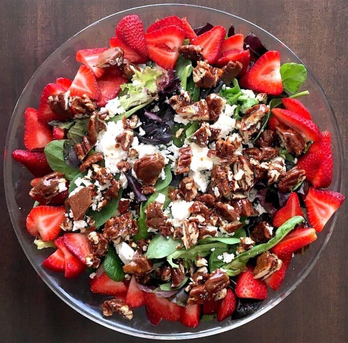 Overhead shot of a vibrant spring salad with strawberry vinaigrette, goat cheese, and pecans