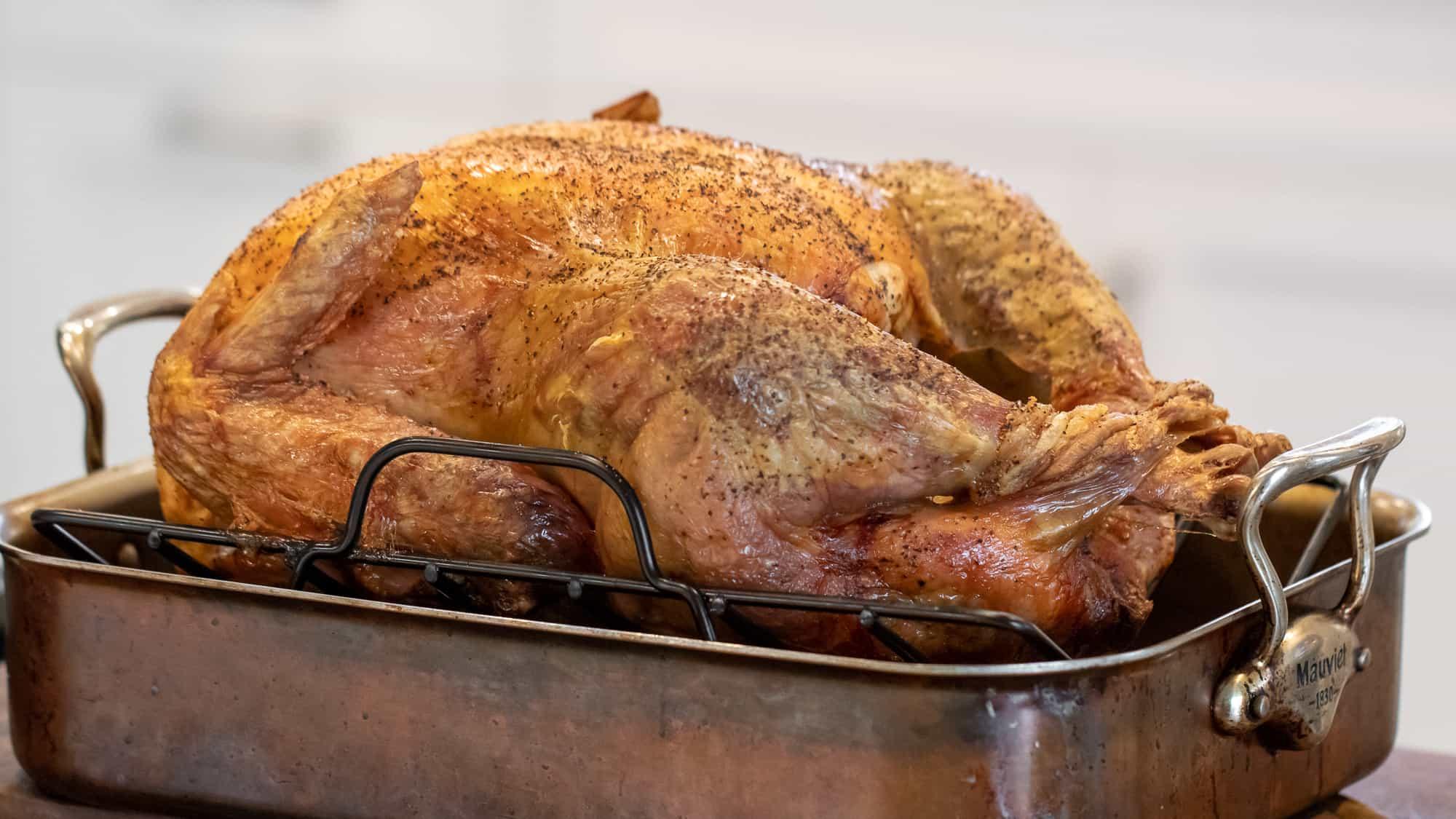 A large roasting pan with a perfectly browned peppercorn crusted turkey being removed from the oven