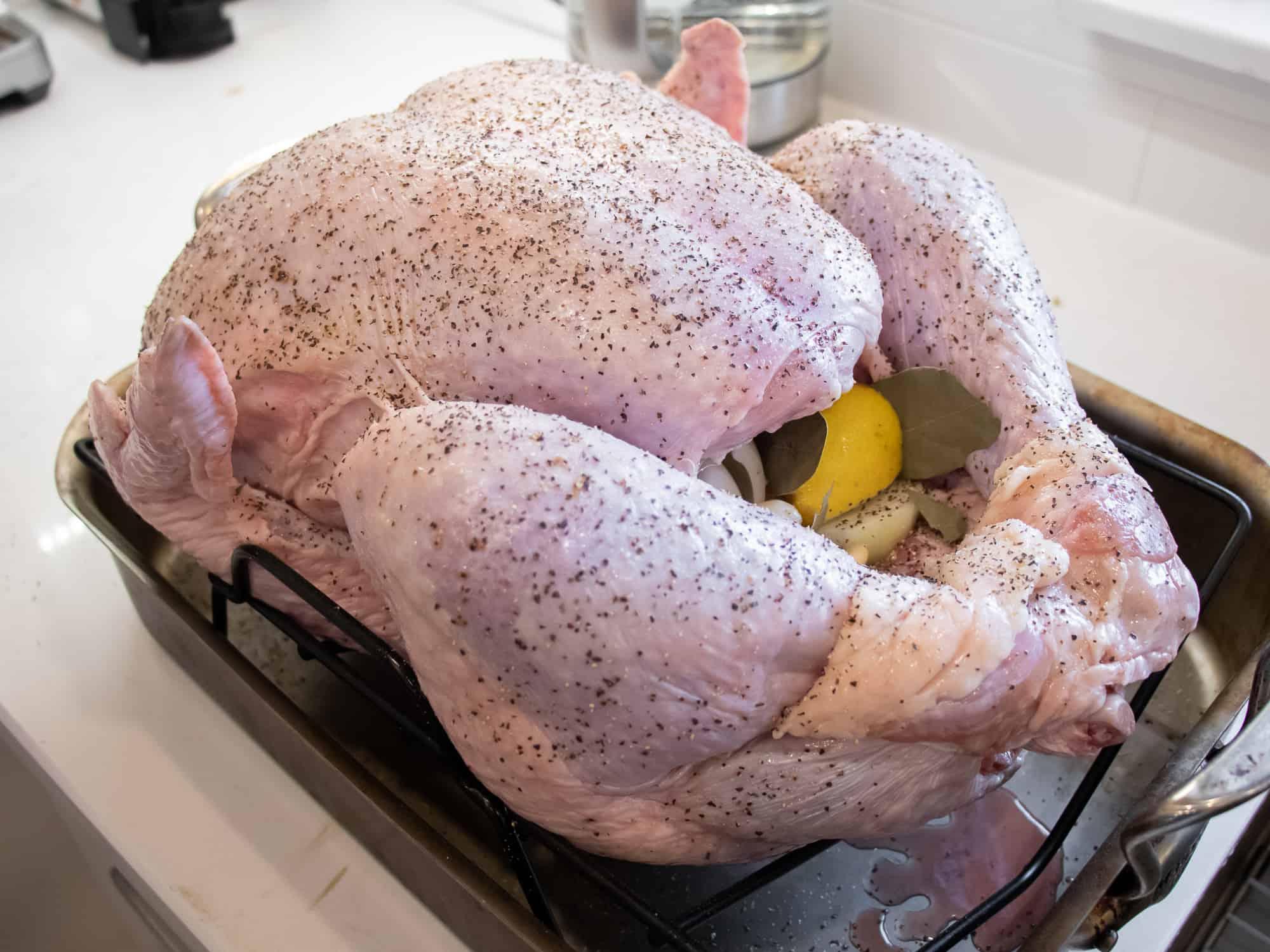 raw turkey being prepared with peppercorn rub