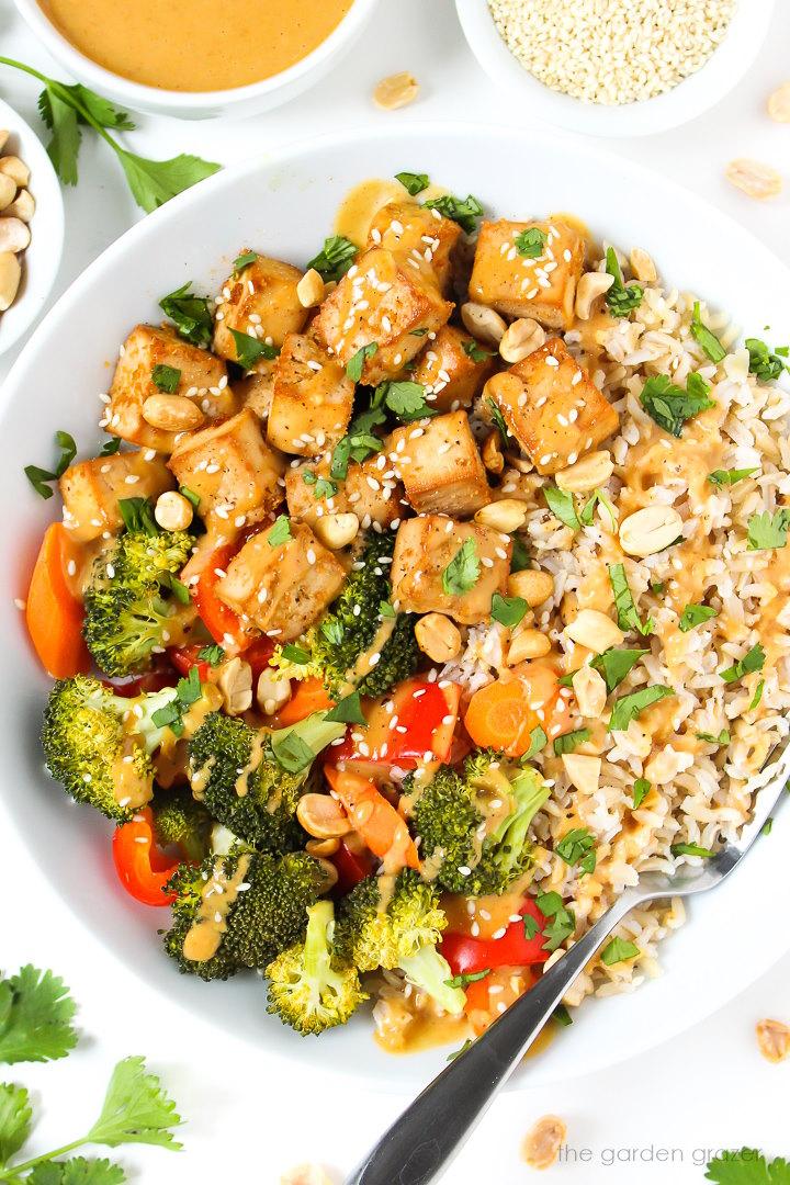 asian inspired tofu rice bowl with crispy tofu, bell peppers, red onion, and peanut sauce