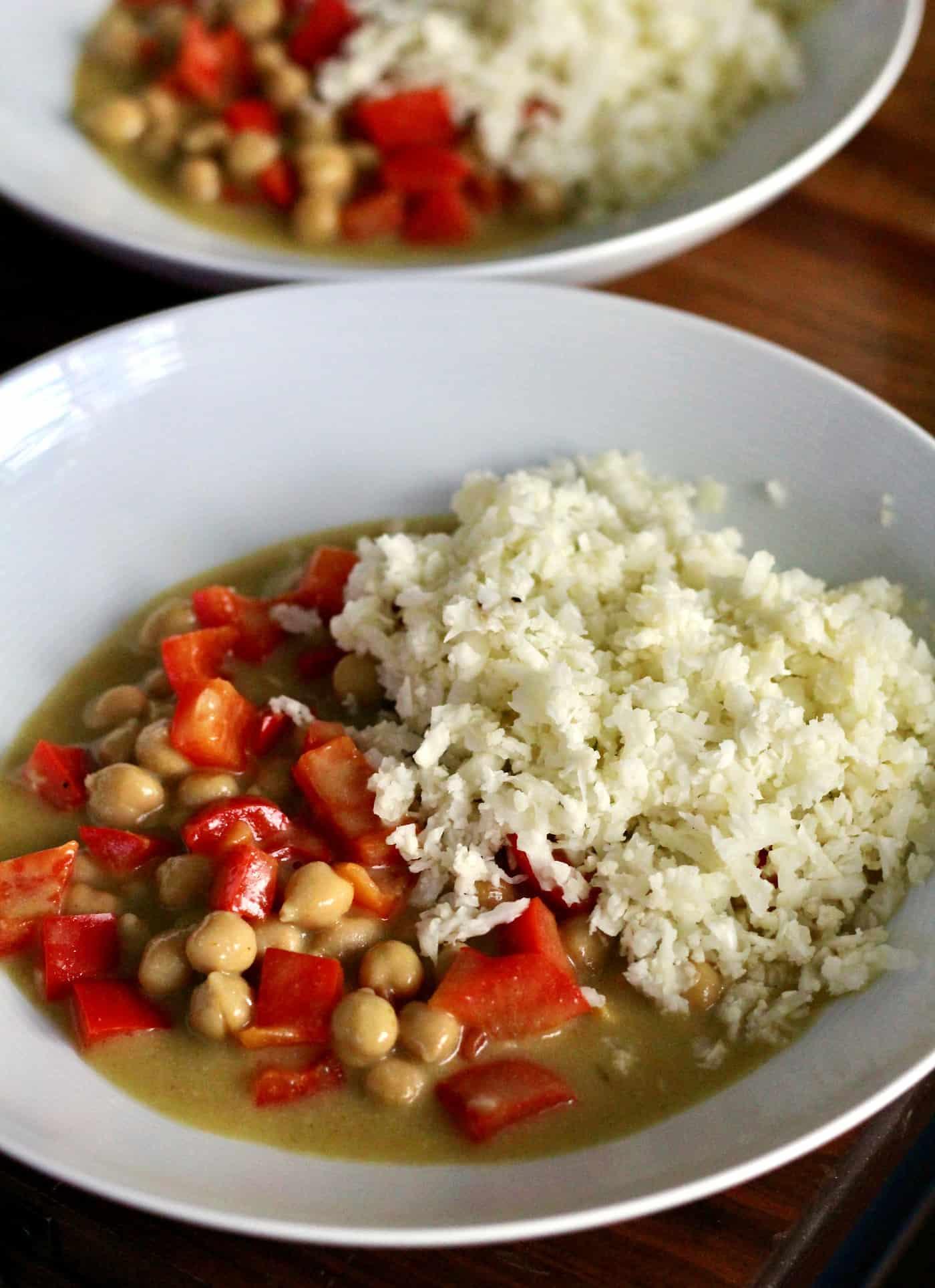 a person holding a bowl of curried chickpea cauliflower rice in a kitchen setting