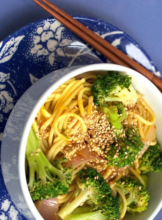 close-up of a hand sprinkling sesame seeds on a bowl of curry udon