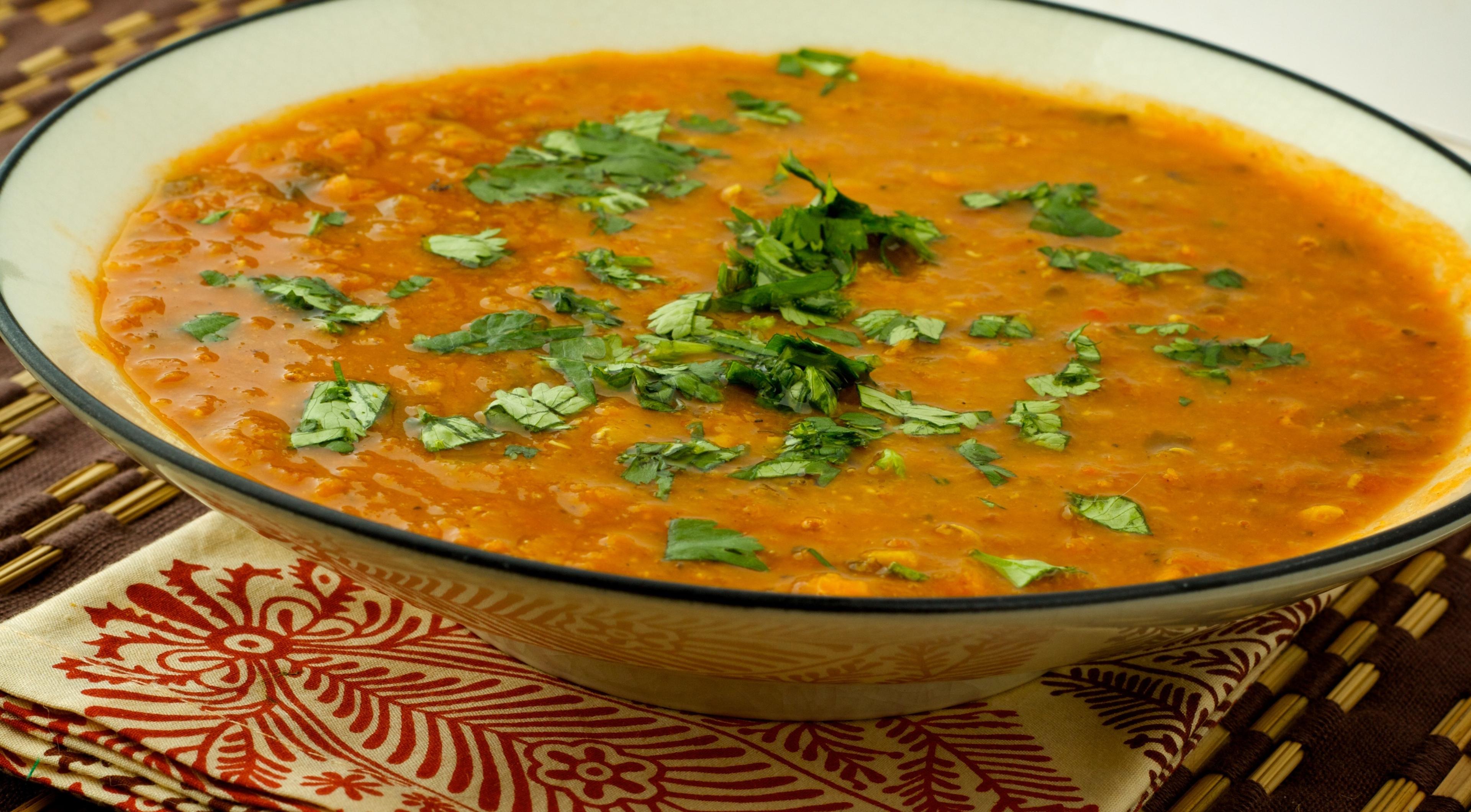 A person enjoying a bowl of lentil soup, sitting by a fireplace