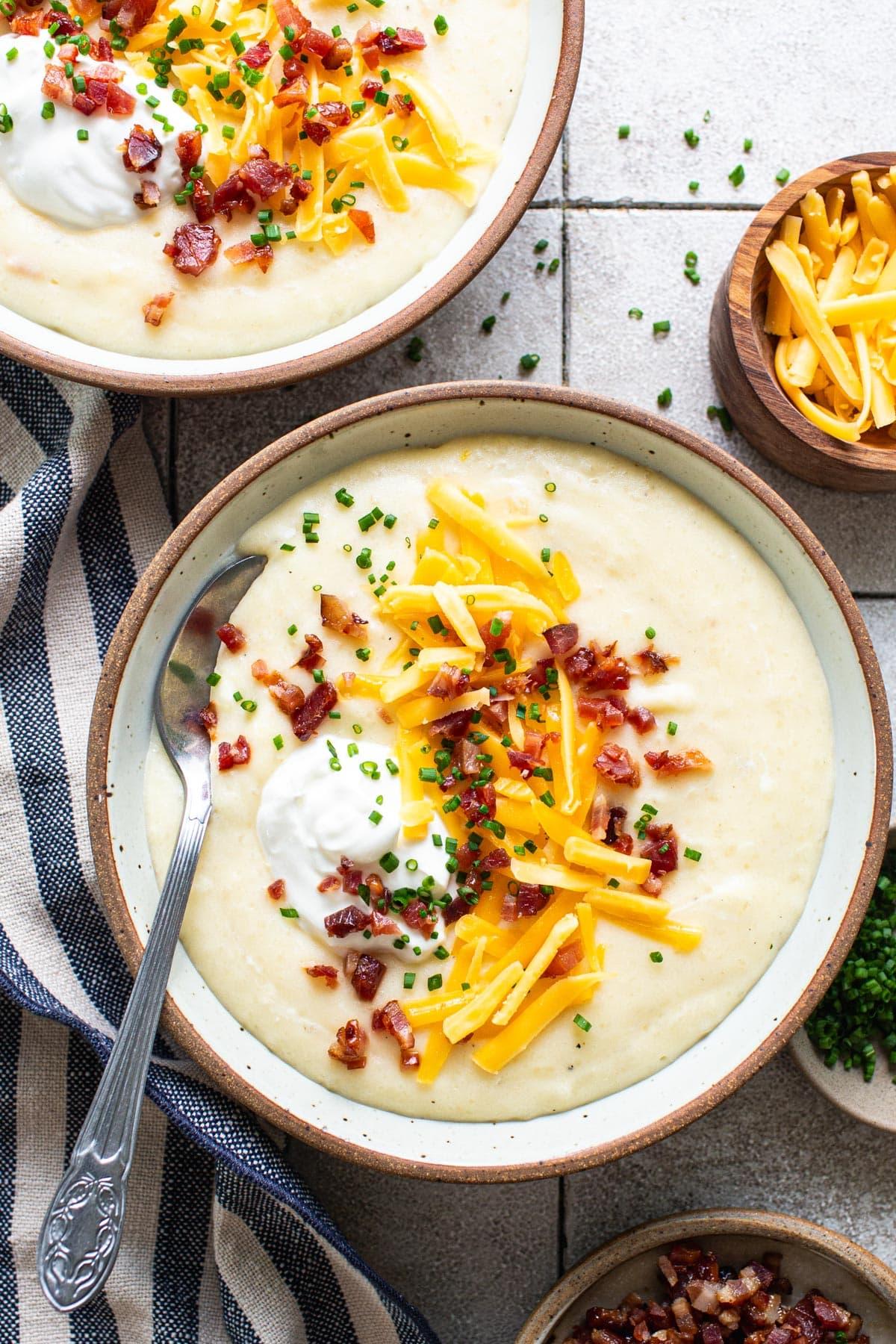 Overhead shot of a rustic table setting with multiple bowls of potato bacon soup and crusty bread
