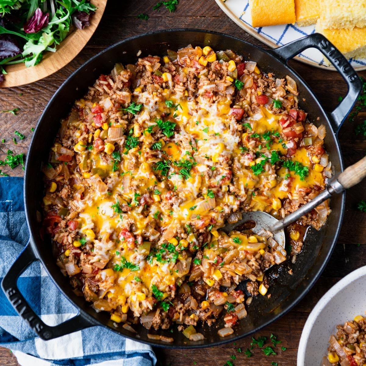 Overhead view of a sizzling ground beef ranch skillet with melted cheddar cheese and fresh green onions, rustic kitchen setting