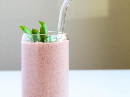 a close-up shot of a vibrant basil and strawberry smoothie being poured into a tall glass