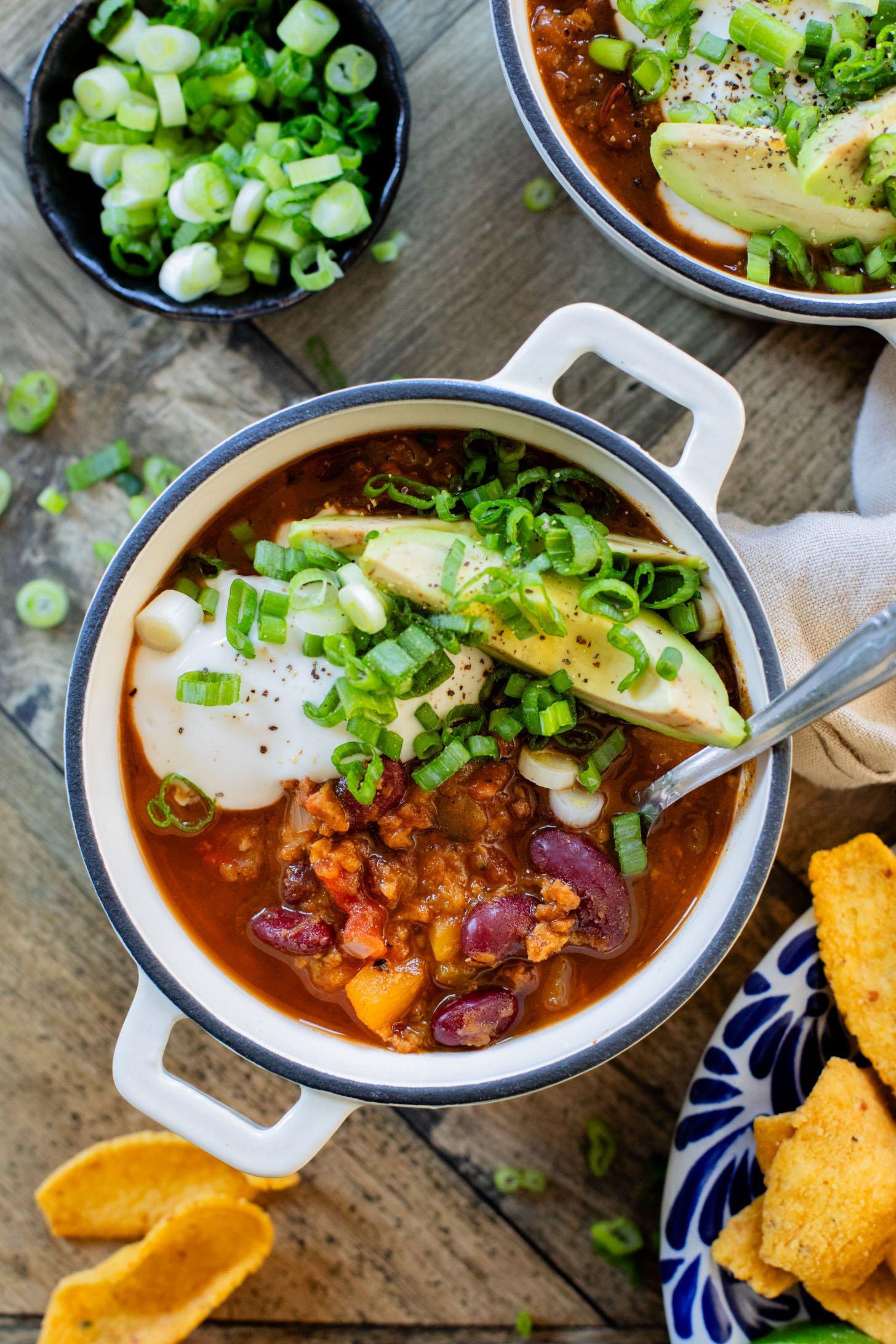 A hearty and vibrant slow cooker butternut squash chili in a rustic bowl, garnished with cilantro and sour cream.