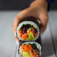 Hands carefully assembling a honeydew sushi burrito with colorful fillings