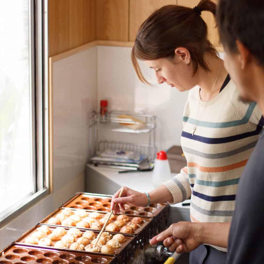 A home cook smiling while making takoyaki in their kitchen