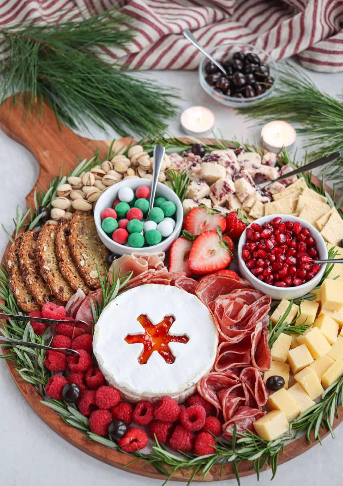 Rustic wooden charcuterie board with baked camembert in the center, surrounded by colorful meats and fruits