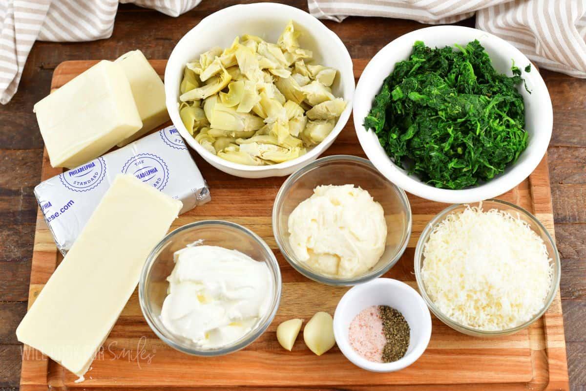 ingredients for spinach artichoke dip laid out on a wooden board