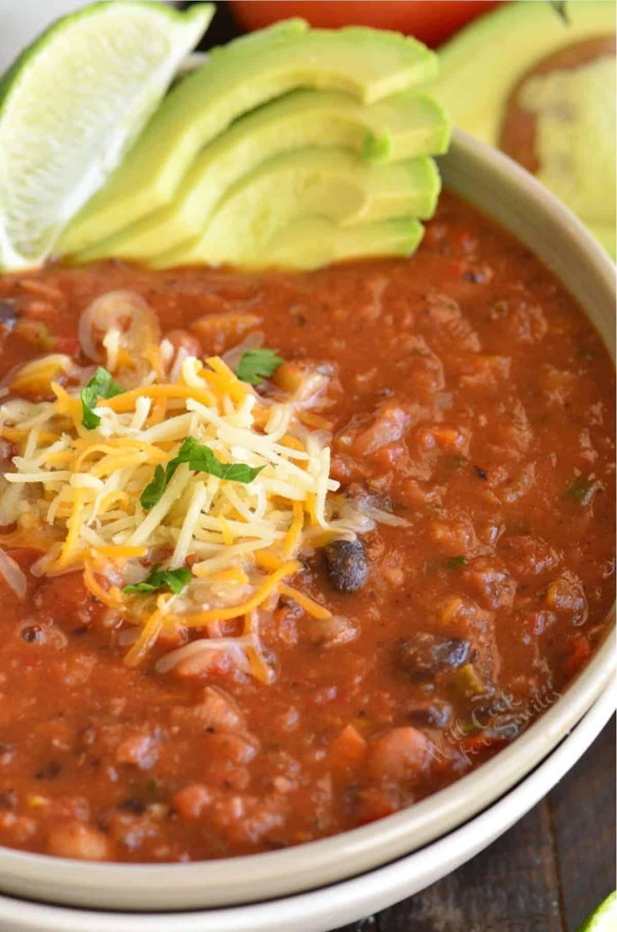 Close-up of a steaming bowl of vegetarian chili, garnished with fresh herbs and a sprinkle of cheese.