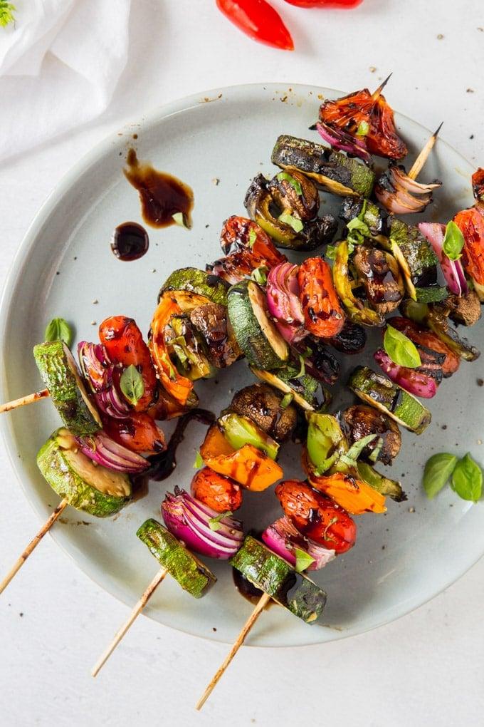 Overhead shot of a platter of grilled vegetable souvlaki skewers with a bowl of balsamic vinaigrette