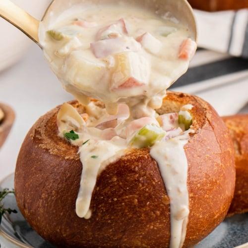 steaming bowl of clam chowder being poured into a toasted bagel bowl