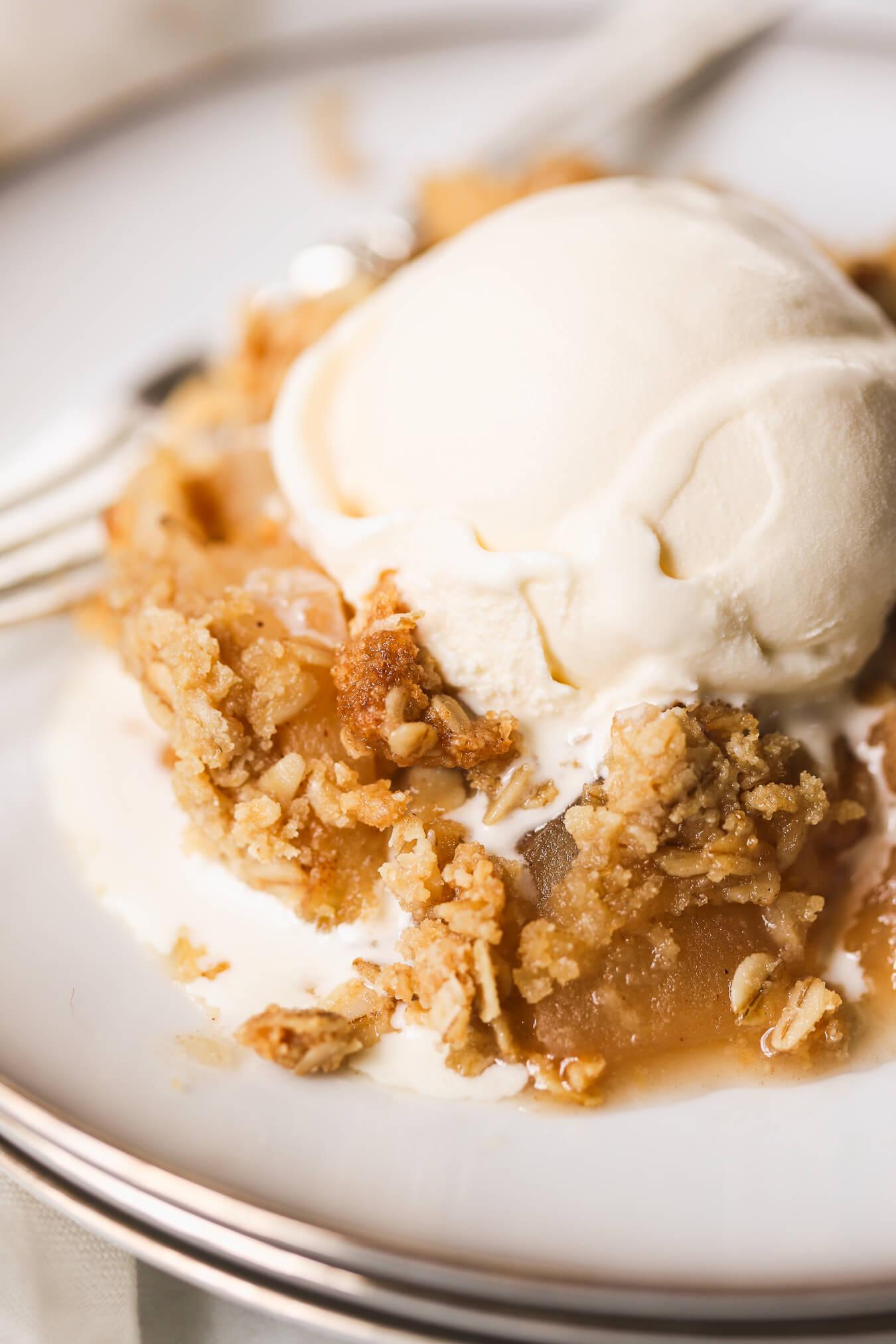A rustic, close-up shot of warm apple crisp oatmeal in a baking dish, garnished with cinnamon and a scoop of vanilla ice cream
