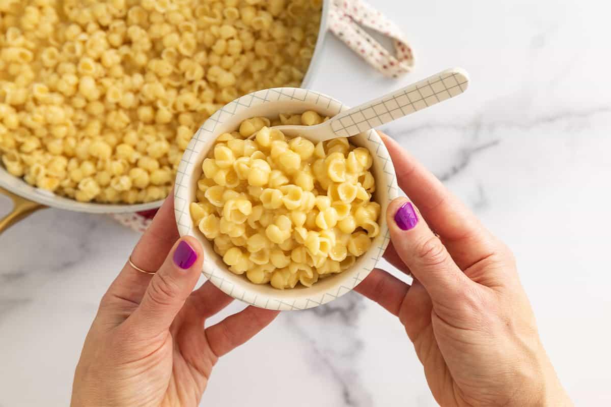 Hands serving a portion of mac and cheese crust pot into a bowl, warm lighting