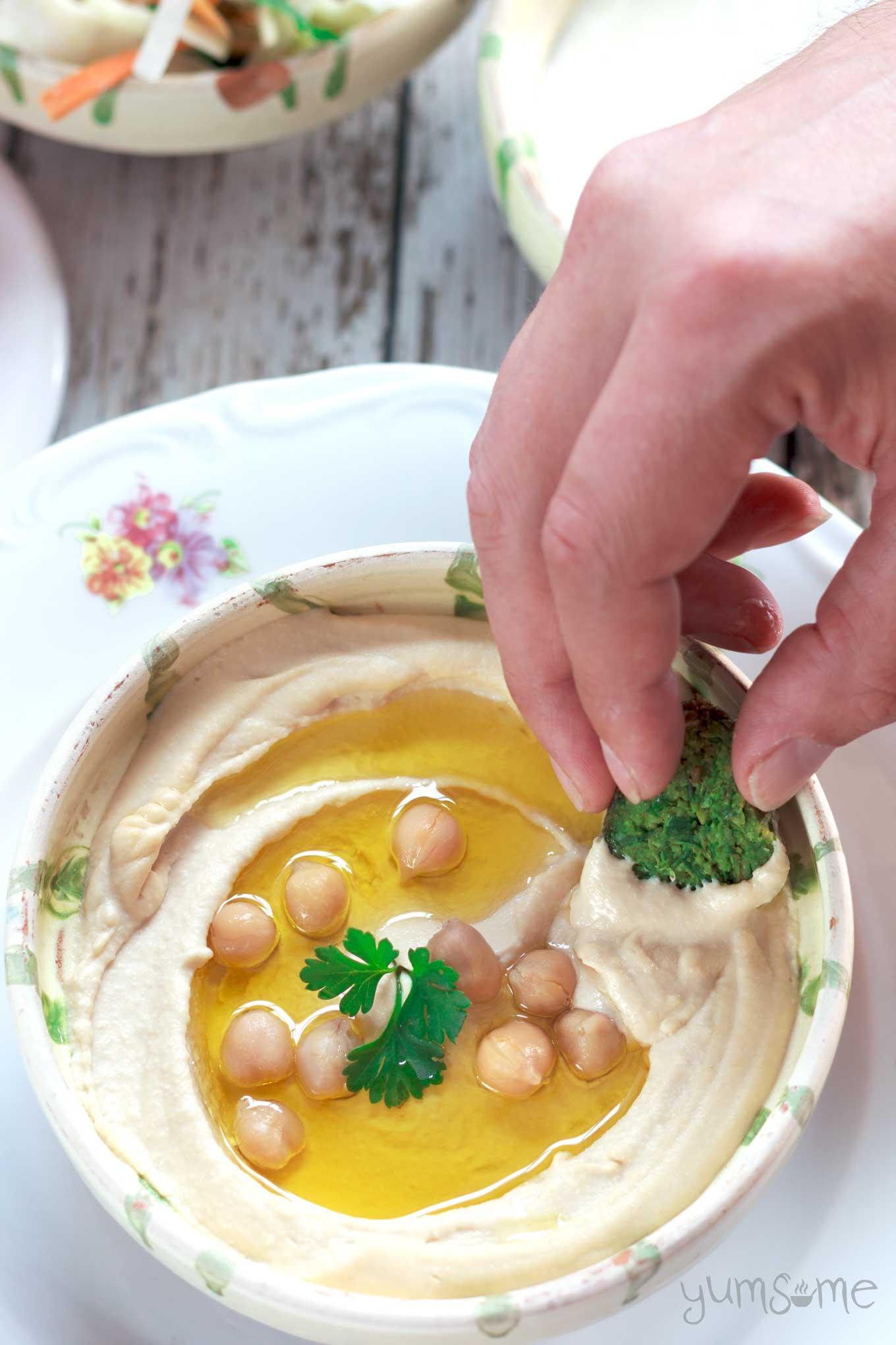 Close up shot of a hand scooping creamy hummus with a multigrain chip