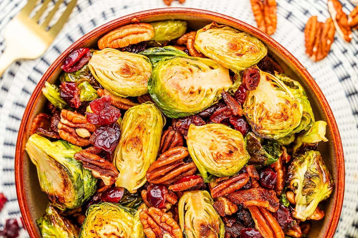 overhead view of a large wooden bowl filled with brussels sprouts salad, cranberries, and pecans