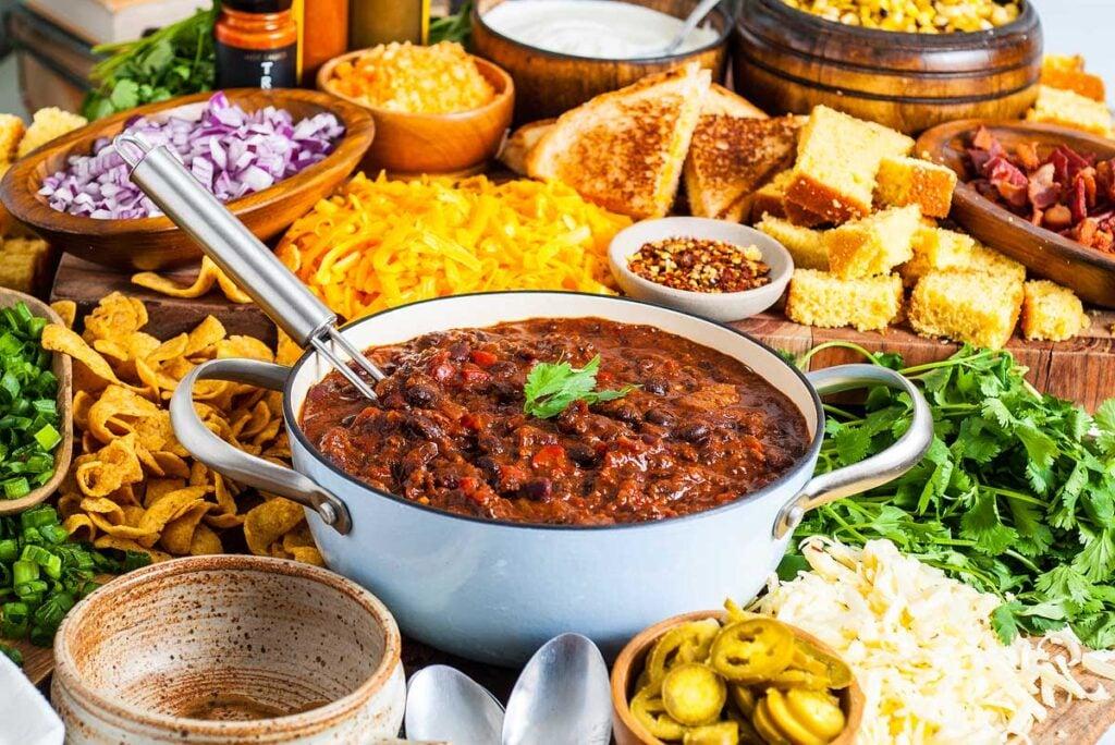 a rustic table setting with bowls of chili, cornbread, and various toppings