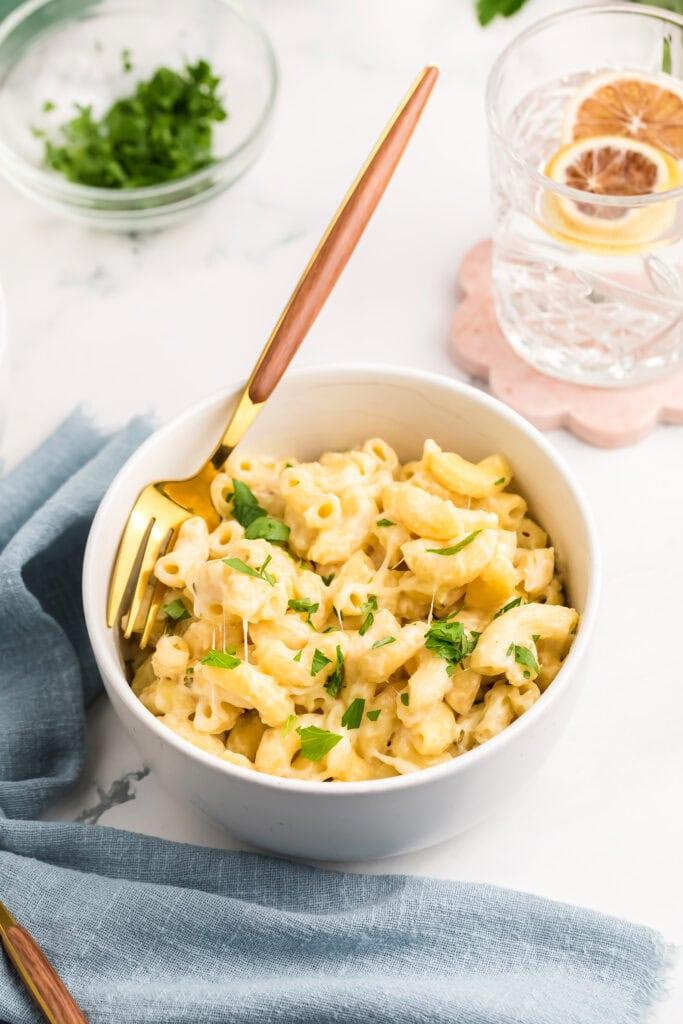 A person serving a generous portion of cream-top mac and cheese into a bowl, garnished with fresh parsley