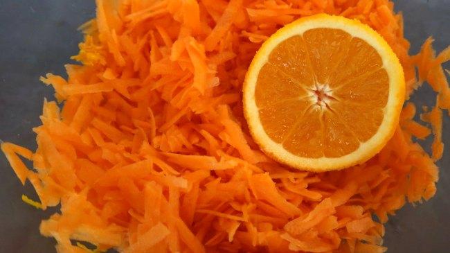 close-up shot of grated carrots and orange segments being tossed together in a bowl