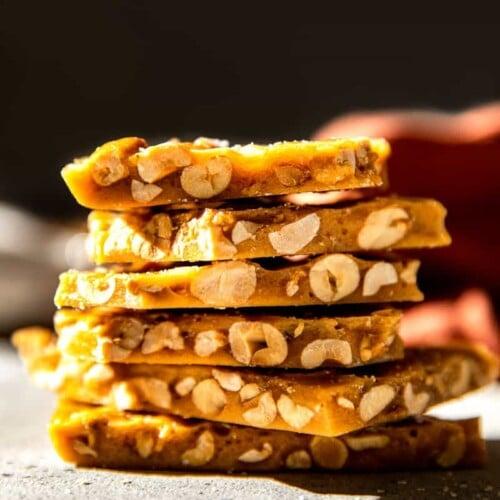 Close-up of a broken piece of peanut brittle showcasing its glossy, amber texture and perfectly embedded roasted peanuts, on a white background.