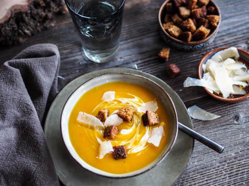 bowl of gingerbread spiced pumpkin soup with a swirl of cream and gingerbread croutons
