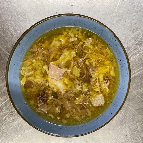 A hearty bowl of pork and cabbage soup with steam rising, garnished with fresh parsley