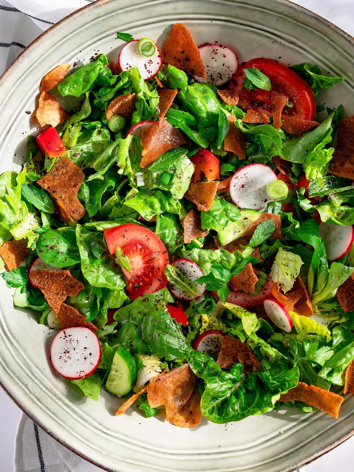 A vibrant, colorful bowl of Bruneian Fattoush salad, showcasing the crisp vegetables and toasted pita bread.