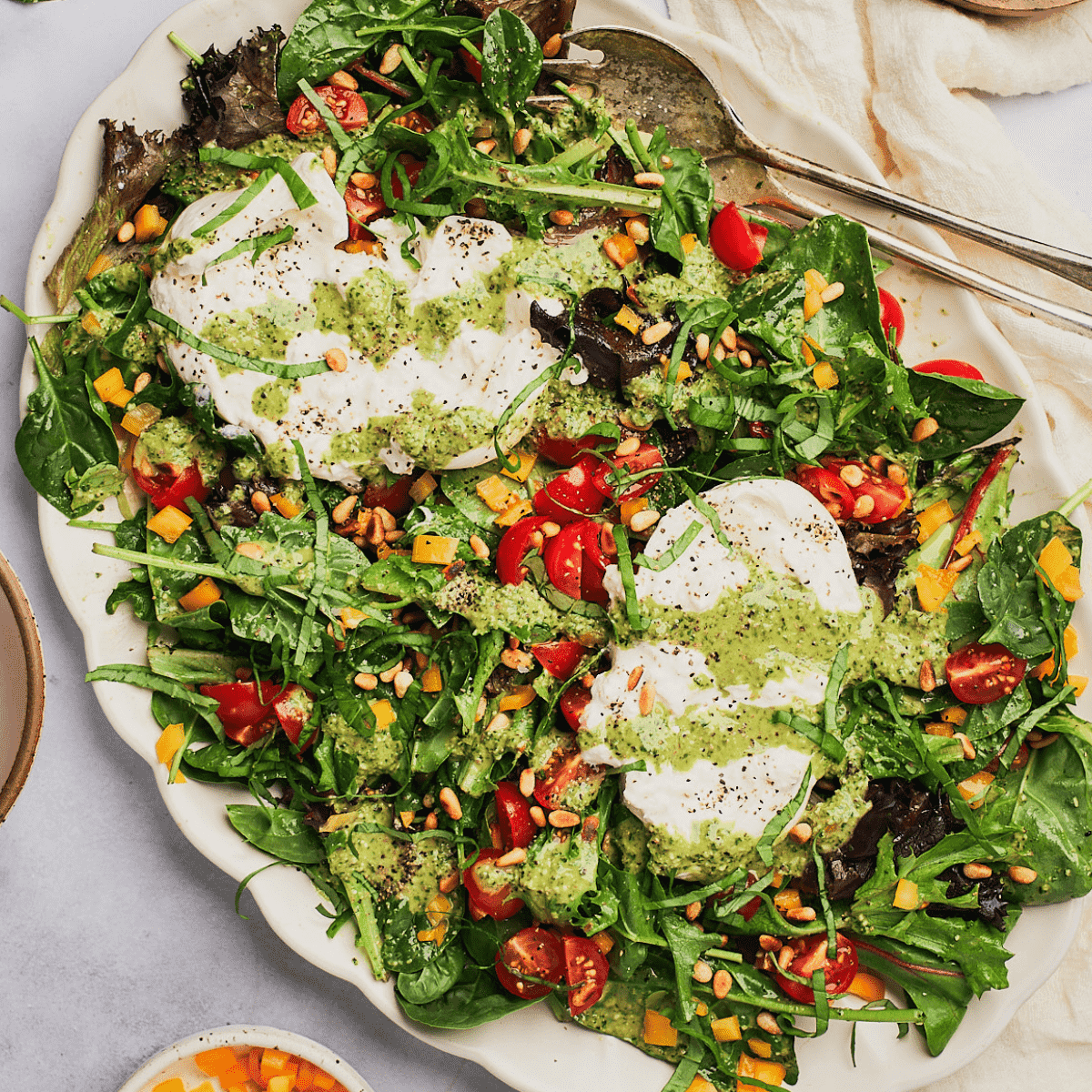Close-up of a vibrant fattoush salad with creamy burrata cheese and vibrant green pesto, garnished with fresh herbs