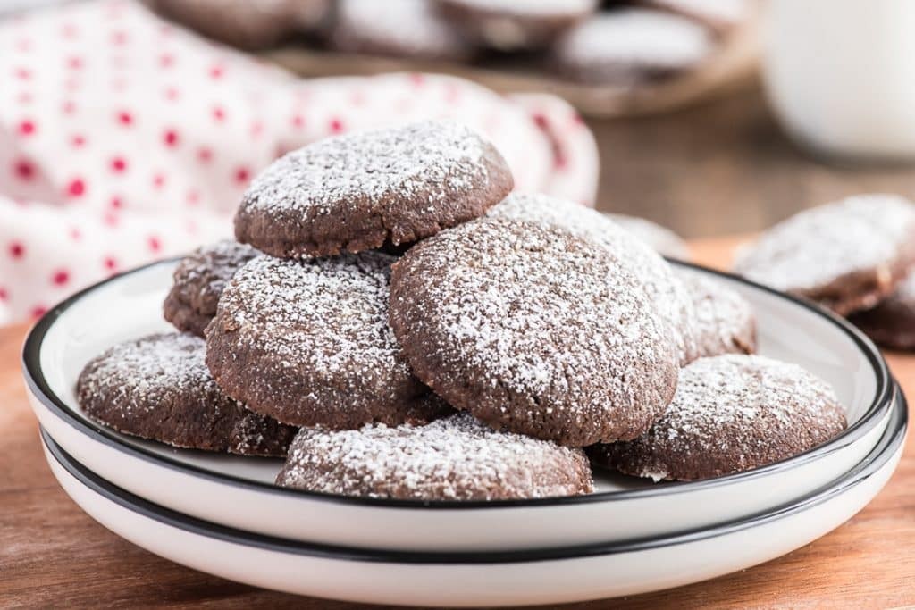 Gourmet dark cocoa sugar cookies with a dusting of powdered sugar on a vintage plate, close-up, warm lighting