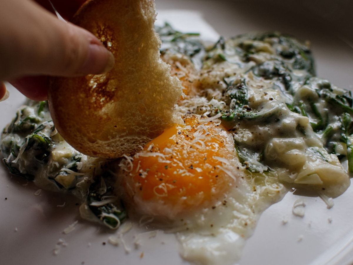 Close-up shot of golden brown Florentine Eggs in a skillet, showing creamy yolks and wilted spinach