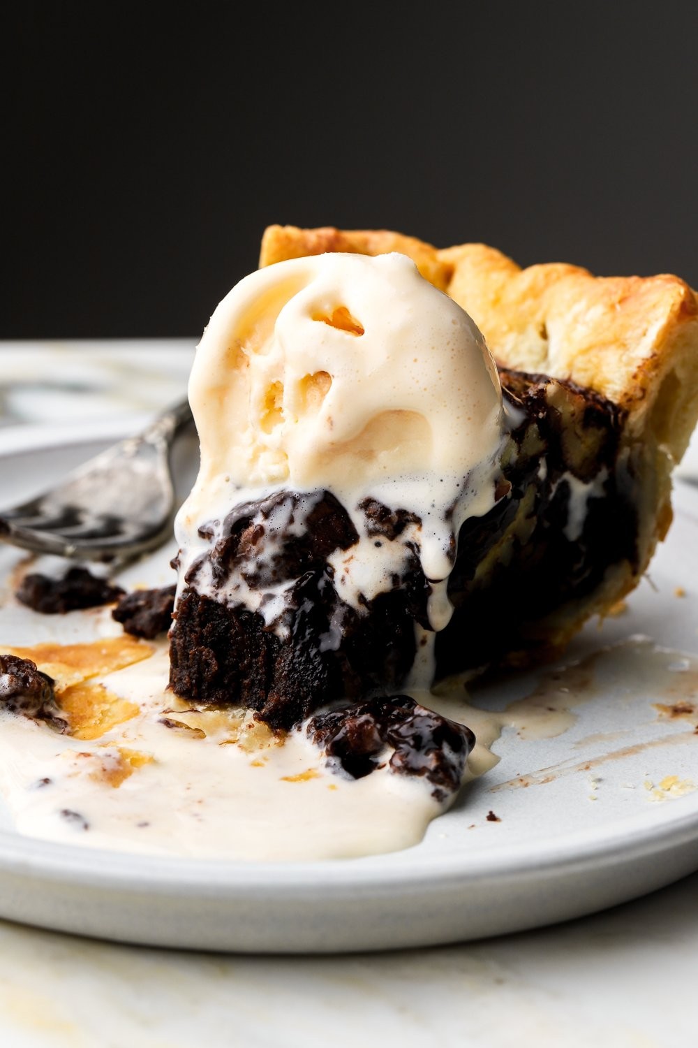 Close up of a slice of warm chocolate pecan pie with a fudgy center, served with vanilla ice cream