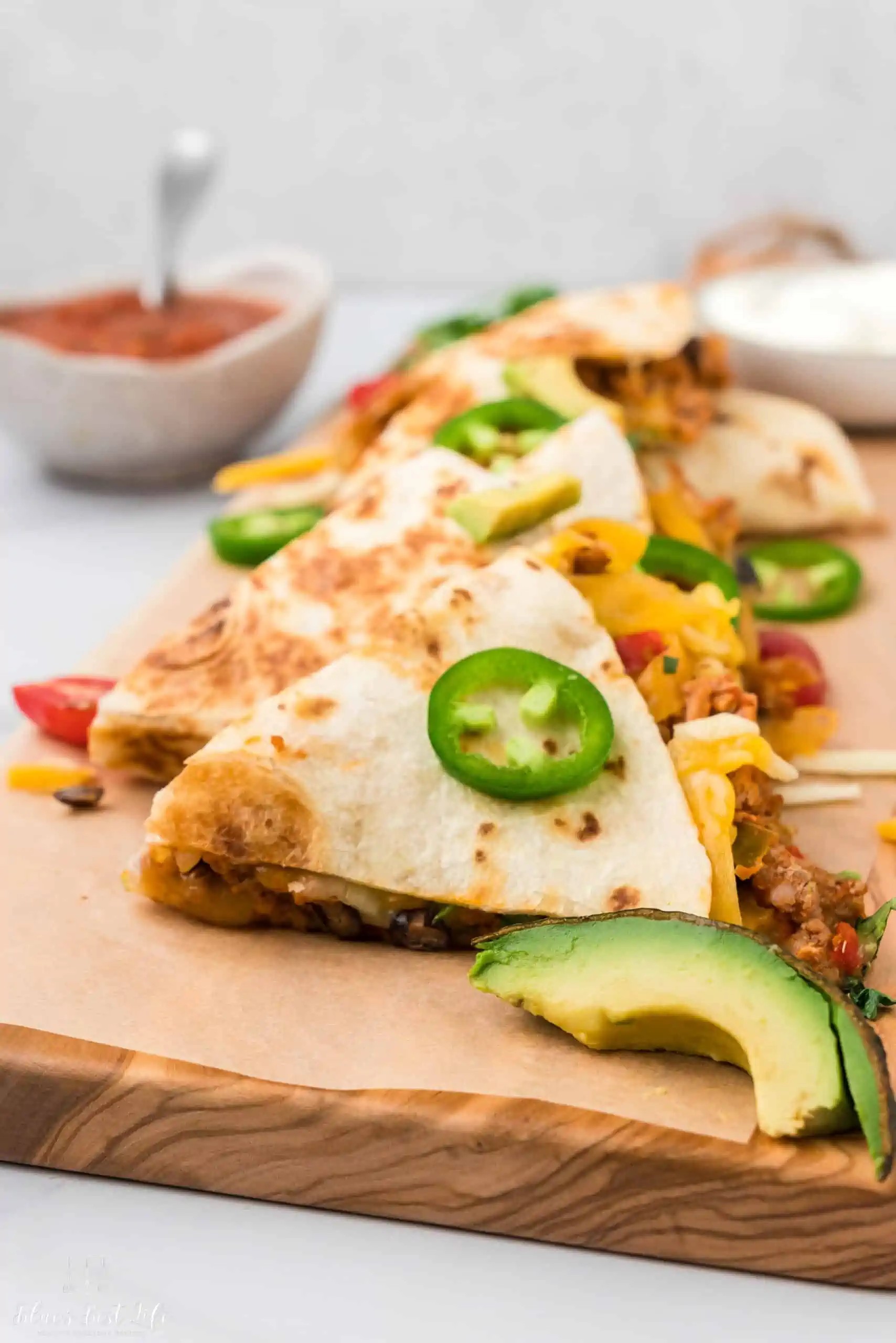 Close-up shot of two turkey quesadillas with avocado crema drizzled on top, served with a side of salsa