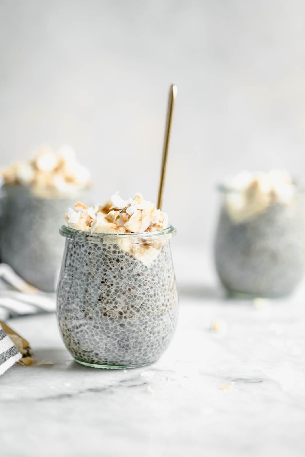 A close-up shot of a creamy, light-brown chia pudding layered with toasted coconut flakes and a lime wedge