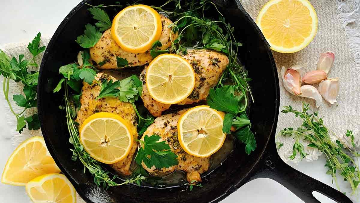 Lemon herb chicken sizzling in a cast iron skillet with fresh parsley garnish