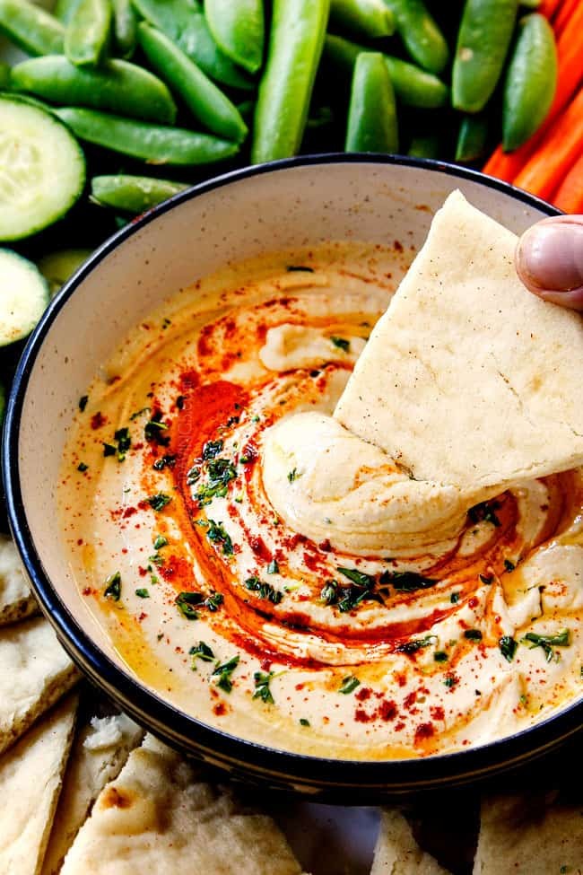 Close-up shot of creamy hummus with capers, drizzled with olive oil, served with pita bread.