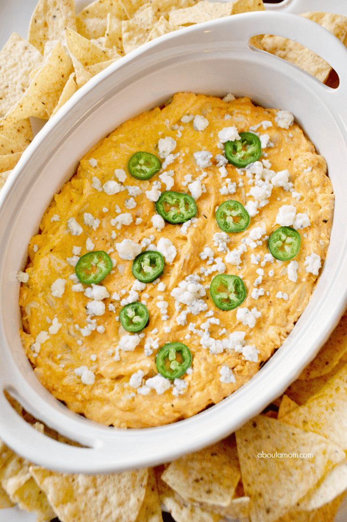 Creamy, bubbling buffalo chicken dip in a slow cooker, surrounded by tortilla chips and celery sticks at a lively party