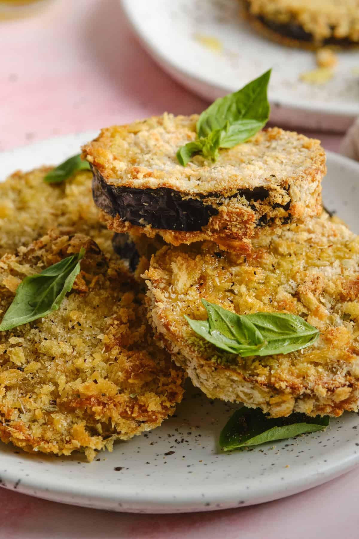 Crispy tempura-fried eggplant slices arranged artfully on a plate, drizzled with vibrant green pesto sauce